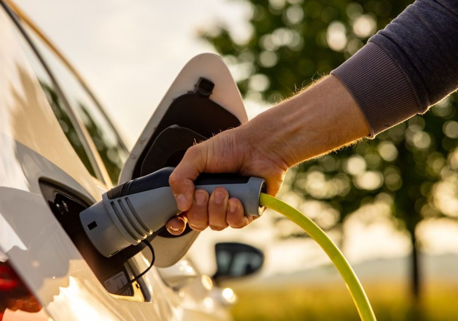 Image showing the arm of a man plugging in a charger into an electric car.