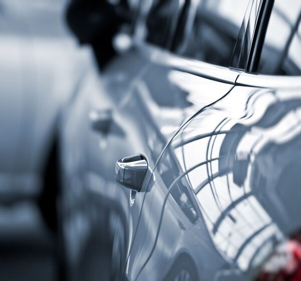 Image showing a close up of the lefthand side of a glossy white luxury car. Close up image of lefthand side of a glossy white luxury car at a dealership with a focus on the handle of the backdoor.
