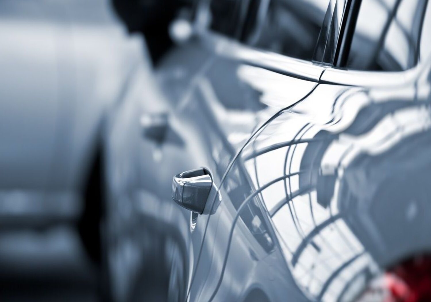 Image showing a close up of the lefthand side of a glossy white luxury car. Close up image of lefthand side of a glossy white luxury car at a dealership with a focus on the handle of the backdoor.