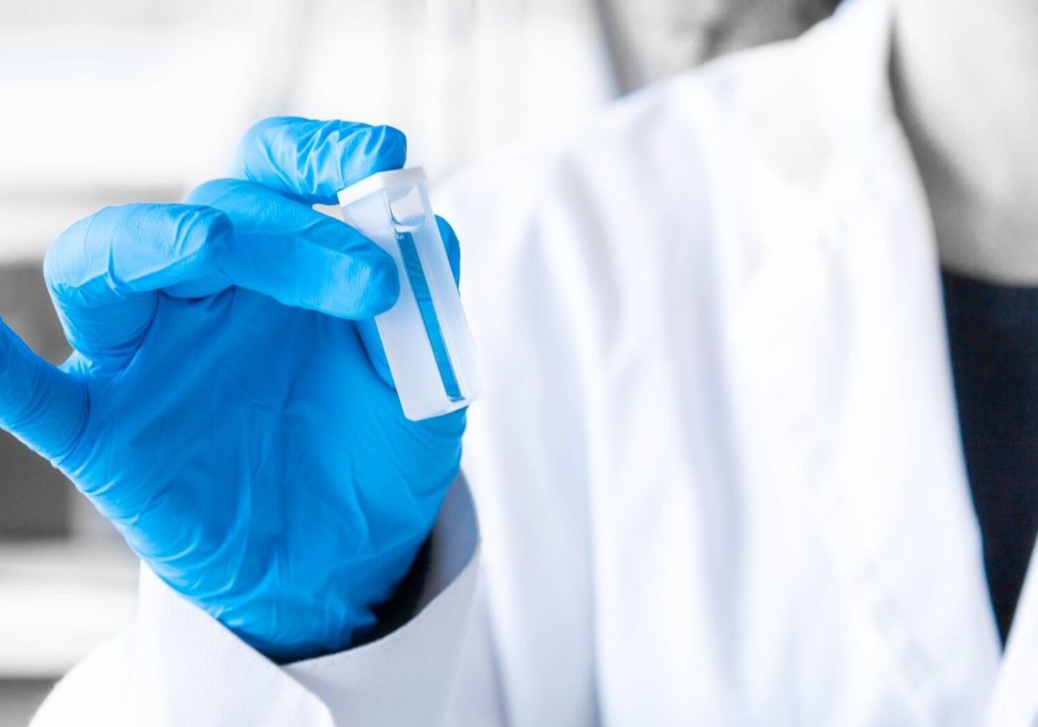 Image showing a scientist holding a spectrophotometry cuvette. Close up of a blue-gloved hand of a scientist holding a transparent spectrophotometry cuvette.