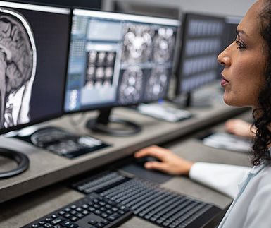 Image showing a hospital technician studying a grey-scale MRI scan of a head on a computer