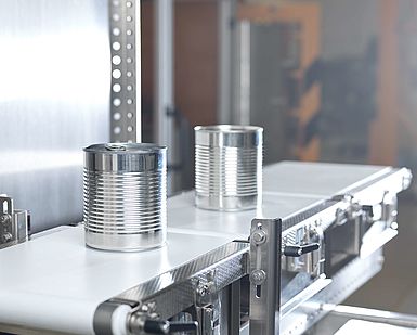 Two metal cans being moved across the conveyer belt of an automatic weighing machine; Copyright: PTB