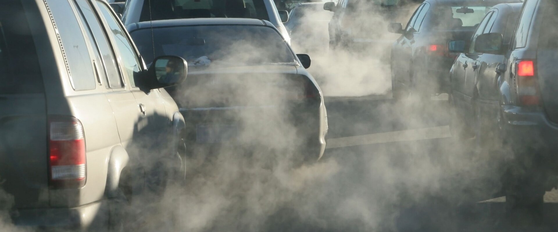 Cars on the road emitting exhaust fumes A photograph of a number of cars stopped at a traffic slight. The image is hazy with exhaust fumes coming from the vehicles’ exhausts