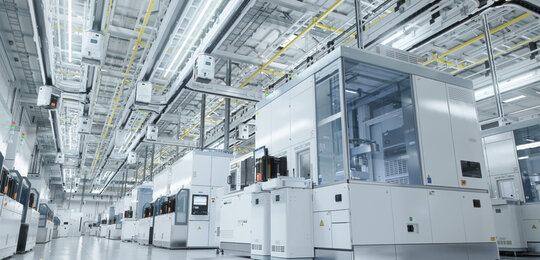 In a grey and sterile warehouse a series of enclosed modules producing semiconductors stretch off into the distance