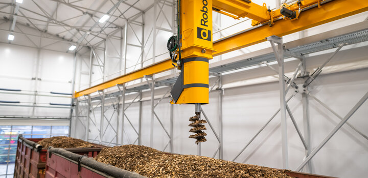 Image showing Q-Robot, a large arm with a screw-shaped sampler on the end, taking a sample from a truck filled with wood shavings