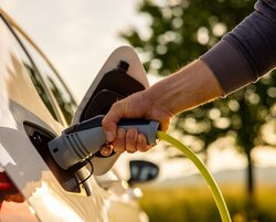 Image showing Hand of man inserting a power cord into an electric car for charging ecofriendly vehicle on green landscape