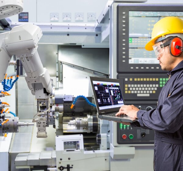 Image showing an engineer using a laptop to  control a robotic arm  performing maintenance