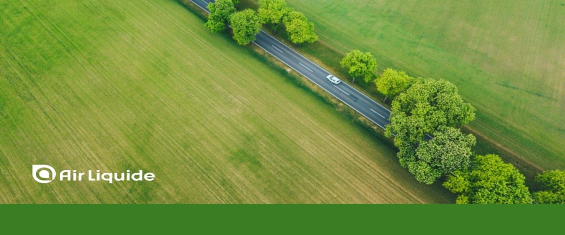 Courtesy Air Liquide Image showing an arial view of a car driving down a road lined by trees and surrounded by green fields. Along the bottom is written “Air Liquide” and the company is credited for image on the left-hand side of the picture.