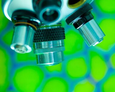 Close up of the lenses of a traditional microscope against a green background