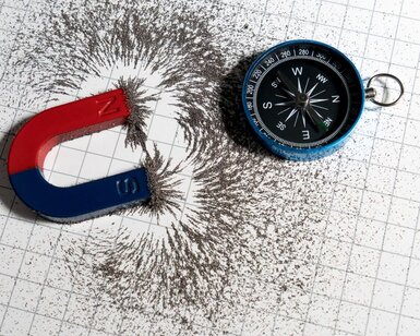 Image showing red and blue horseshoe magnet or physics magnetic and compass with iron powder magnetic field on white paper graph background