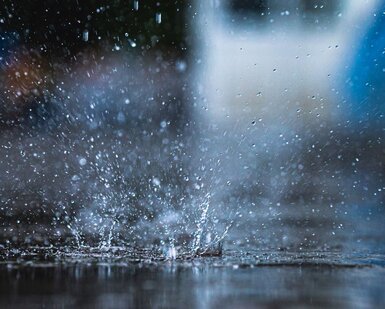 Image showing rain falling into a puddle, causing a splash of water