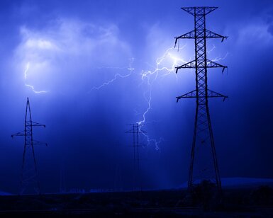 White lightning bolts light up a night sky against illuminating a series of electricity pylons 