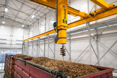 Image showing Q-Robot, a large arm with a screw-shaped sampler on the end, taking a sample from a truck filled with wood shavings