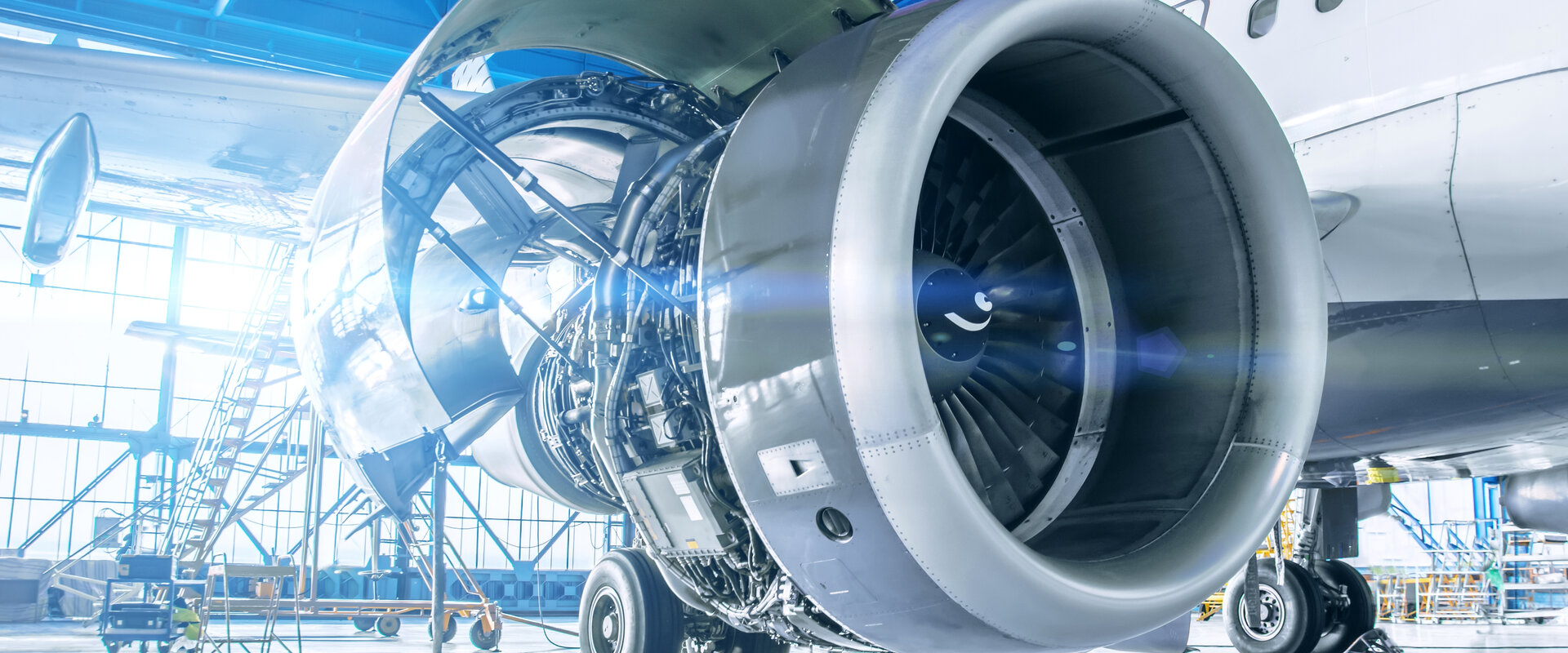 Close up image of maintenance being performed on the exposed engine of an aircraft inside a large hanger