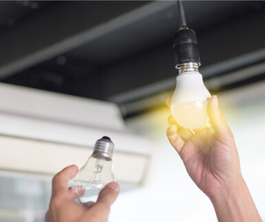 Power saving concept. Consumer changing compact-fluorescent (CFL) bulbs with new LED light bulb