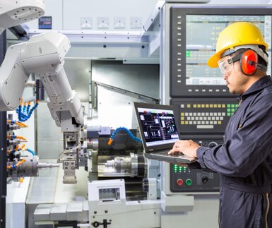Image showing an engineer using a laptop to  control a robotic arm  performing maintenance
