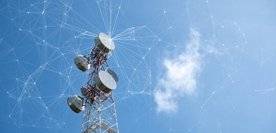 Against a clear blue sky is the steel frame of a telecommunication tower with dishes sending out signals that are displayed as an interconnected “wireframe”