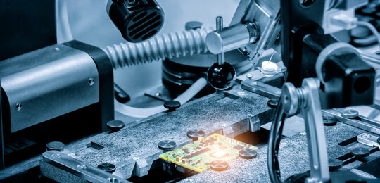 A grey and silver image of a silicon chip surrounded by various testing equipment