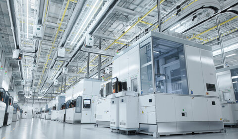 In a grey and sterile warehouse a series of enclosed modules producing semiconductors stretch off into the distance