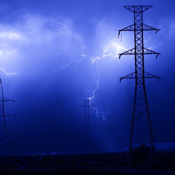 White lightning bolts light up a night sky against illuminating a series of electricity pylons 