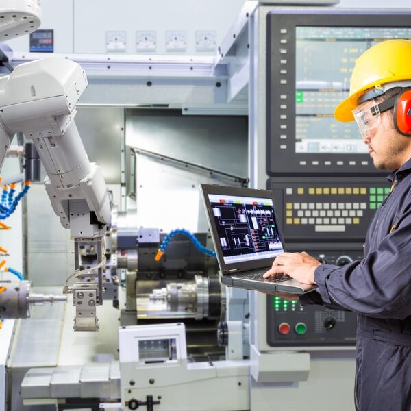 Image showing an engineer using a laptop to  control a robotic arm  performing maintenance