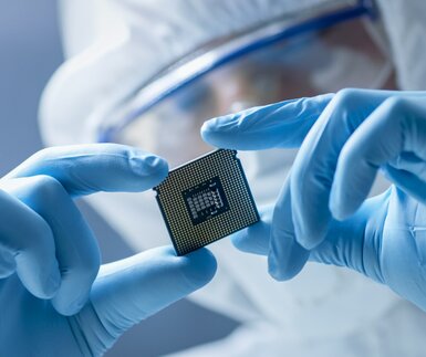 Image showing engineer in sterile coverall holding microchip with gloves and examining it