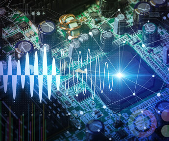 Close up of an electronic circuit board with transistors and connections overlayed with a graphic of a sine-wave representing the flow of digital information