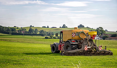 In the early morning light a tractor in the foreground is spraying pesticide over rows of low plants in a large open field