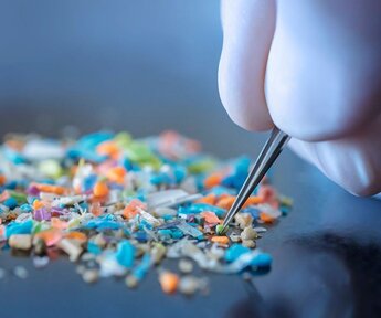 Image showing a person with medical gloves and tweezers inspecting a pile of microplastics