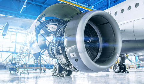 Close up image of maintenance being performed on the exposed engine of an aircraft inside a large hanger
