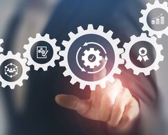 Image showing a person in a business suit pointing to a graphic showing interconnected cogs which each contain an icon of a different industry concept