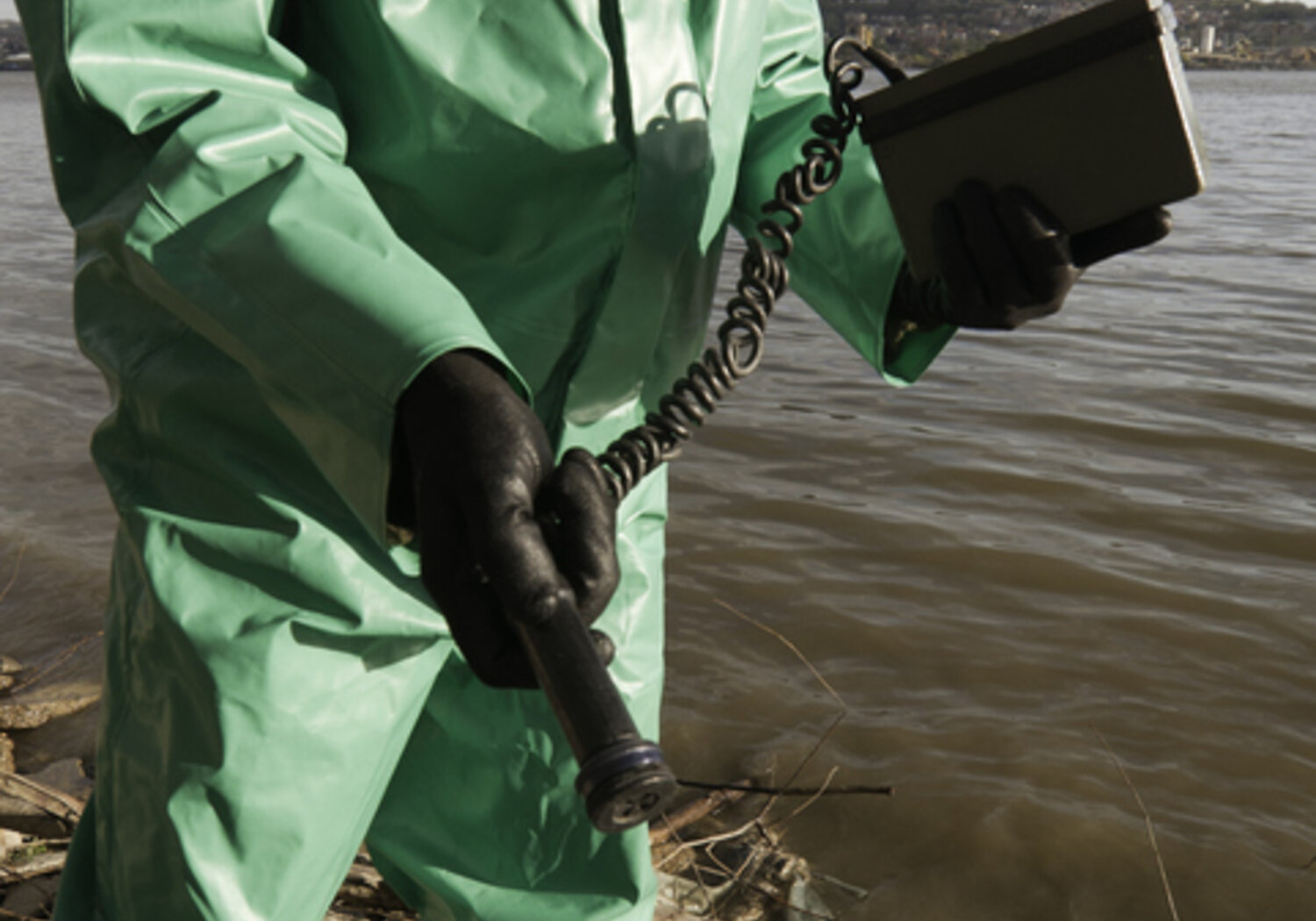 Image showing a person in a green protective covering with a gas mask holding a geiger counter
