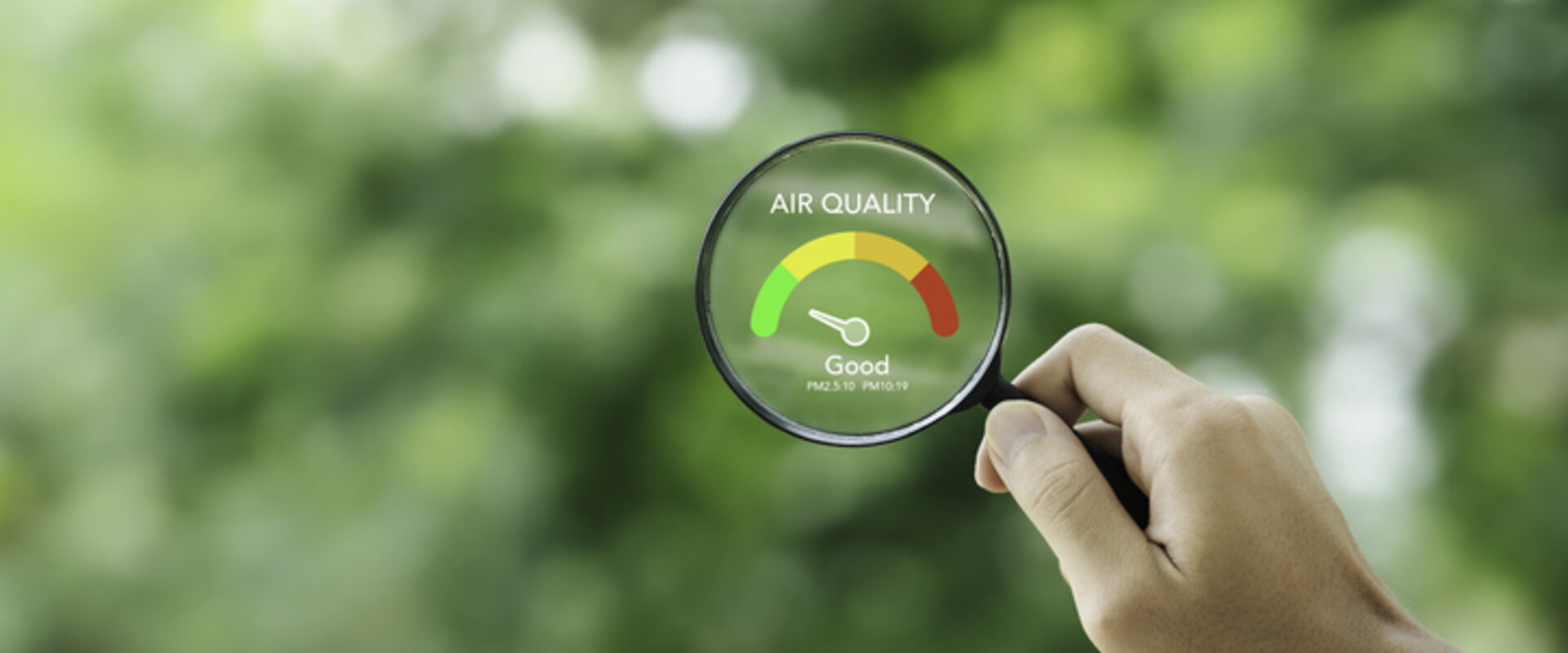 Measuring atmospheric air quality Against a blurry background of trees, in the foreground is a hand holding a magnifying glass with the words “Air quality – Good” in its centre
