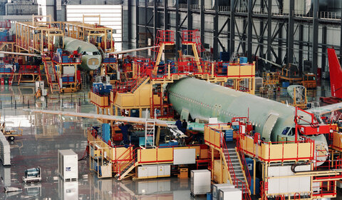 In a vast indoor hanger two commercial aircraft, surrounded by gantries and equipment, are being assembled