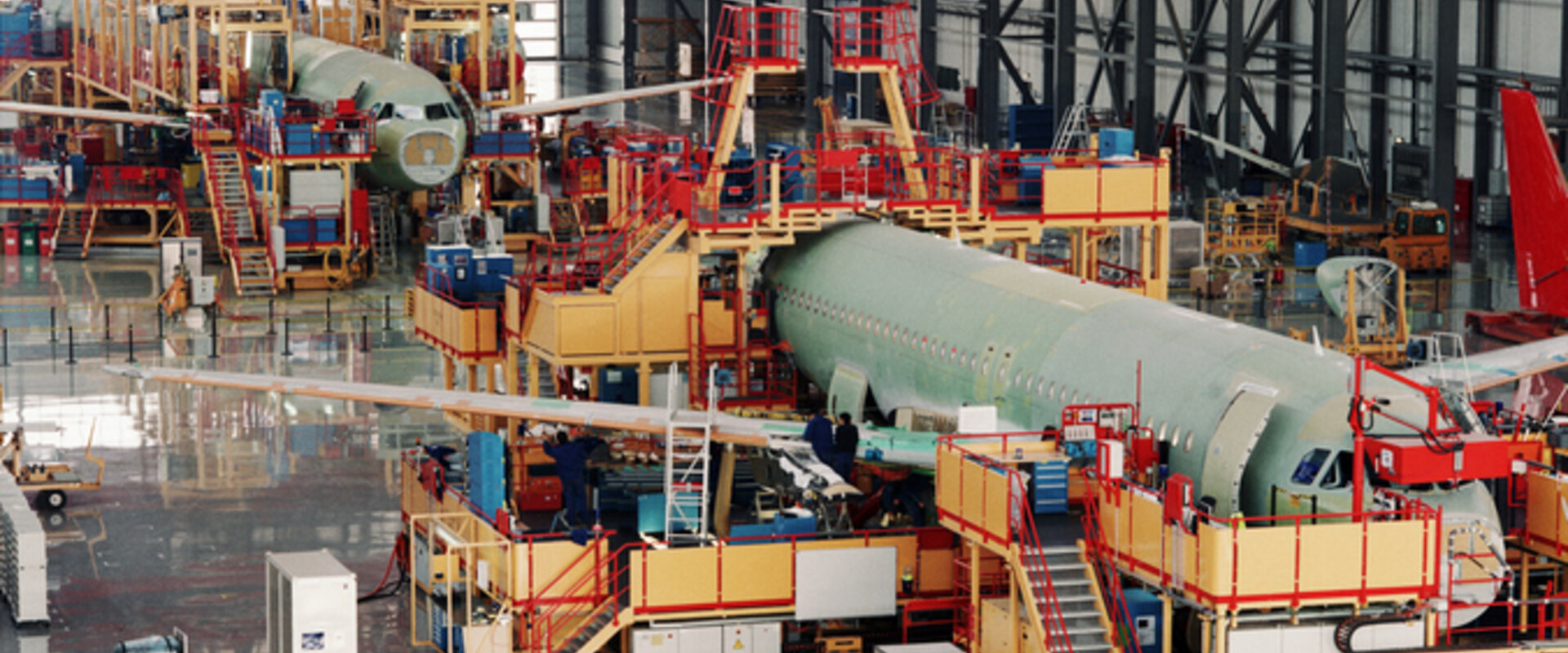 An aircraft assembly line In a vast indoor hanger two commercial aircraft, surrounded by gantries and equipment, are being assembled
