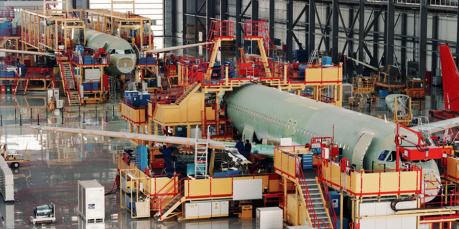 In a vast indoor hanger two commercial aircraft, surrounded by gantries and equipment, are being assembled