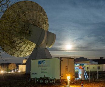 Image showing the measurement trailer and the TeleYAG-II interferometer mounted on a surveying pillar in front of a radio telescope and two satellite-laser-ranging domes at the Geodetic Observatory Wettzell, Germany
