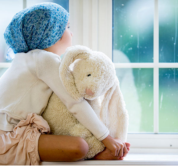 Image of a small child with toy sitting at a windowsill