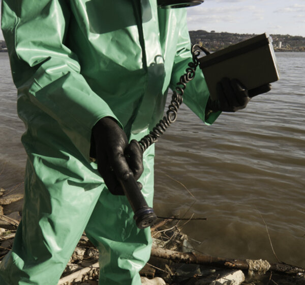 Image showing a person in a green protective covering with a gas mask holding a geiger counter