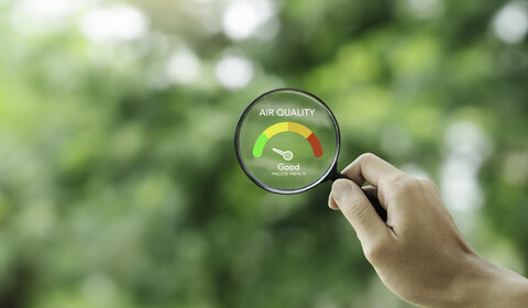 Against a blurry background of trees, in the foreground is a hand holding a magnifying glass with the words “Air quality – Good” in its centre