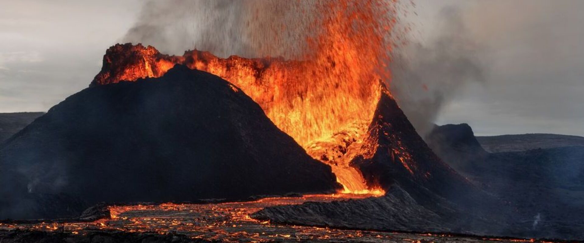Erupting volcano in Iceland In the foreground is an erupting volcano in Iceland with a lava flow descending its flank