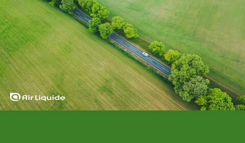 Image showing an arial view of a car driving down a road lined by trees and surrounded by green fields. Along the bottom is written “Air Liquide” and the company is credited for image on the left-hand side of the picture.